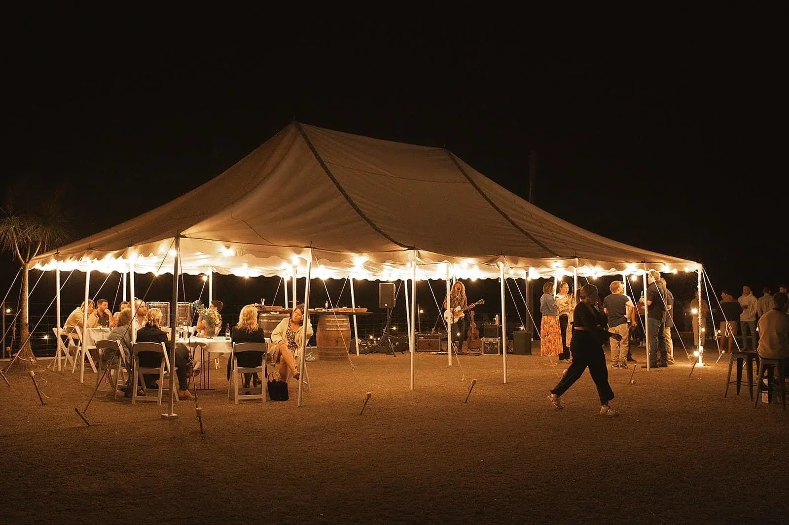 Peg-and-pole marquee at night with festoon lights and guests seated at tables